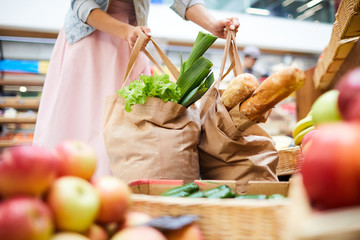 close-up of unrecognizable woman in skirt standing in food organic store and picking heavy shopping 