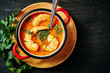 traditional Thai soup with shrimp and coconut milk in a red pot and a spoon with parsley