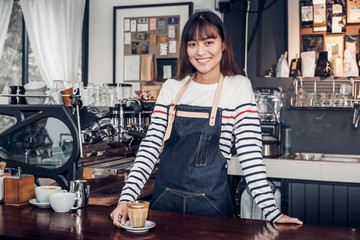 Poster - Asian female barista wear jean apron place her hand on counter bar and smiling to customer,cafe service concept,owner business start up