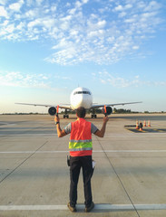 Ground Crew in the signal vest. Aviation Marshall / Supervisor meets passenger airplane at the airport. Aircraft is taxiing to the parking place.