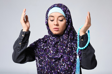 Wall Mural - Young Muslim woman praying on light background