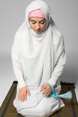 Wall Mural - Young Muslim woman praying on light background