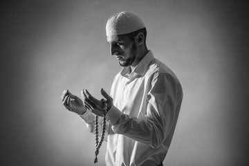 Black and white portrait of young Muslim man praying on dark background