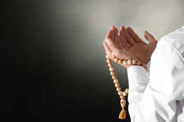 Wall Mural - Young Muslim man with rosary beads praying on dark background, closeup