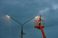 Municipal Worker With Helmet And Safety Protective Equipment Installs New Diode Lights. Worker In Lift Bucket Repair Light Pole. Modernization Of Street Lamps. Technician On Aerial Device. Night Duty