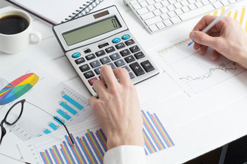 Business man prepares a financial report working with a calculator. Charts for sales reports on the table at the marketing manager.