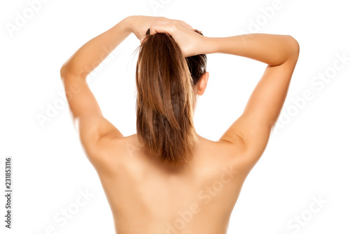Back View Of Young Nude Woman Tying Her Straight Long Hair On