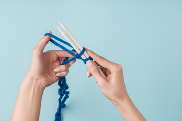 Sticker - partial view of woman with blue yarn and white knitting needles knitting on blue backdrop