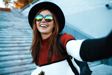 Wall Mural - Cheert! Selfie time! Young happy lady in a spring vacation, walking in the city, drinking coffee, photographing herself on a sunny day,wearing hat and striped sweater.Toned.