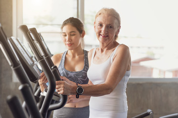 Wall Mural - Trainer with senior woman exercising spinning bike in fitness gym. elderly healthy lifestyle concept.