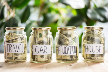 Close-up view of glass jars with dollar banknotes and inscriptions travel, car, education, house