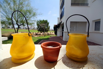 Small yellow and terracotta pots, on a stone ledge, with bright background of a golf course and apartments