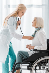 Wall Mural - young female doctor examining with stethoscope disabled senior woman