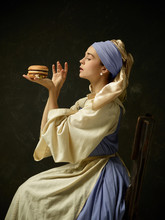 Medieval Woman In Historical Costume Wearing Corset Dress And Bonnet With Burger. Beautiful Peasant Girl Wearing Thrush Costume