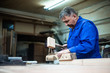 © Vladimir - carpenter working in workshop, a worker planing a tree with a planer