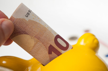 closeup of  hand of man putting ten euros bank note in yellow piggy bank on white background