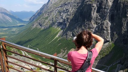 Sticker - Tourist woman with camera taking picture from Trollstigen Trolls Path winding scenic mountain road in Norway Europe. National route. Travel destination