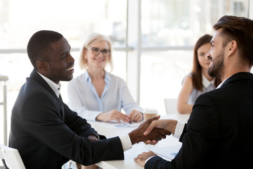 Wall Mural - Caucasian businessman shake hand of black colleague greeting at briefing in office, diverse employees handshake introducing or getting acquainted at meeting, boss congratulate coworker with success