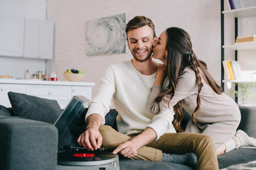 Wall Mural - happy young couple listening music with vinyl record player and cuddling at home