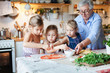 © Marina April - Family, kids cooking pizza in cozy home kitchen. Grandmother and three sisters, her granddaughters preparing homemade italian food. Funny little girls are helping senior woman. Children chef concept.