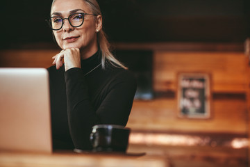 Beautiful mature woman sitting at cafe table with laptop