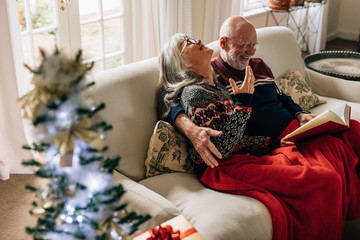 Elderly couple reading a book sitting on sofa at home