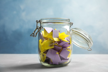 Colorful paper pieces for lottery in glass jar on color background