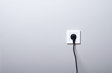 Electric white socket and one plugged in power cord on white wall background