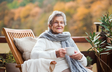 an elderly woman sitting outdoors on a terrace in on a sunny day in autumn.