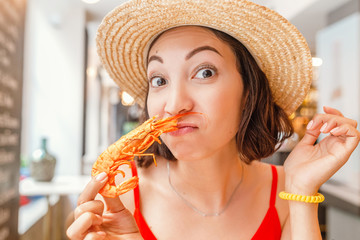 Wall Mural - Happy Asian woman in hat eating local Spanish cuisine grilled seafood