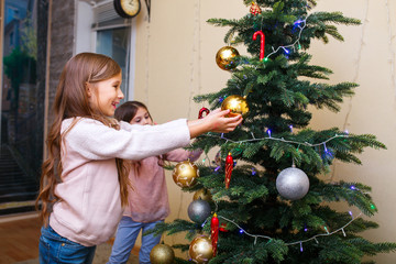 Merry Christmas and Happy Holidays. Two cute little girls are decorating the Christmas tree at home room.