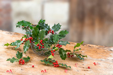 Close Up Iron, Basket Of Holly Red Berries Branches, Grean Leaves, Evergreen, On Rustic, Table Over A , Vintage Ambiance, Frame, On Old Red Brick Wall, Space For Text