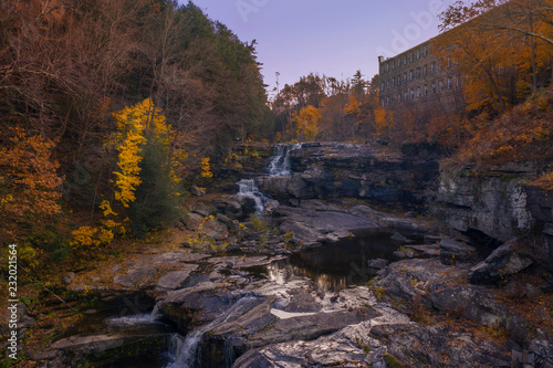 Fotografie, Obraz autumn waterfall scene with trees and old building in background