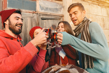 Smiling european men and women during party photoshoot. The guys posing as friends at studio fest with wineglasses with hot mulled wine on foreground.