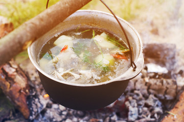 Marching kettle with fish soup over fire in field conditions. Cooking in a backpacking