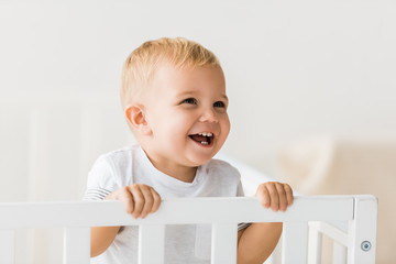 cheerful toddler standing in baby crib on white background