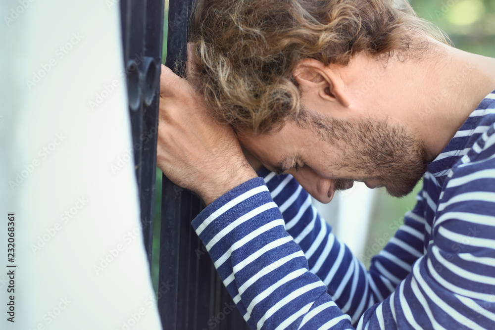 Stressed young man near fence outdoors