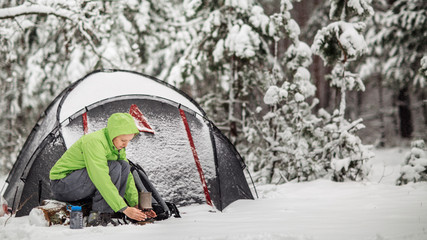 happy woman cooking near winter tent camp in the snow forest.