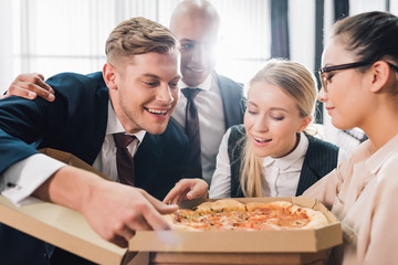 Wall Mural - smiling young coworkers looking at tasty pizza in office