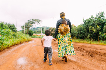 african mother and two children walk alone in red clay road in village as a family in traditional dr