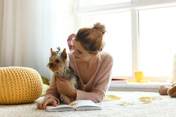 Wall Mural - Woman with cute dog reading book at home on autumn day