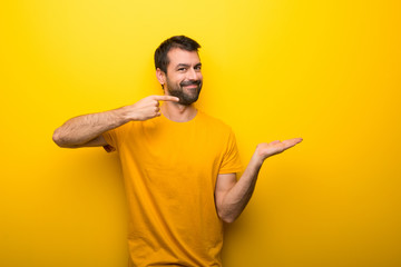 Wall Mural - Man on isolated vibrant yellow color holding copyspace imaginary on the palm to insert an ad