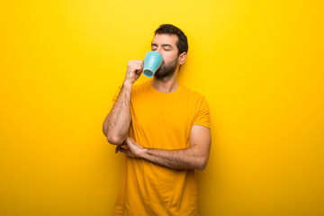 Wall Mural - Man on isolated vibrant yellow color taking a coffee in takeaway paper cup and smiling because he will start the day well