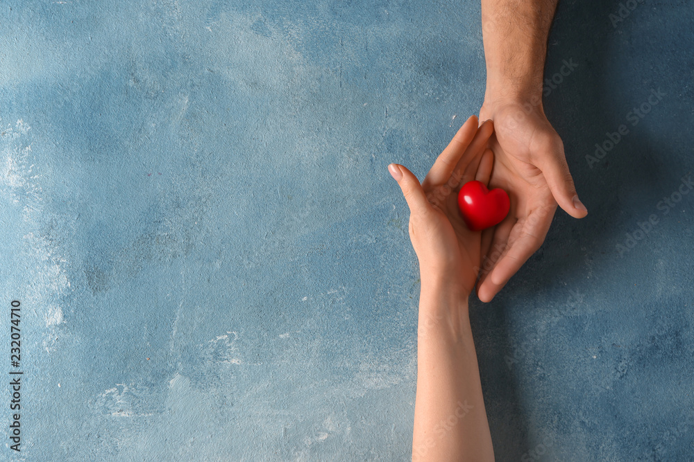 Loving young couple holding red heart on color background