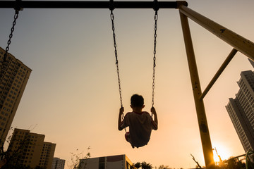 Child swinging on swing in sunset in city with building on background