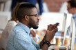 © fizkes - African American male employee in glasses busy with smartphone texting message to friend, serious black worker using cell phone at work browsing internet or checking email or social medias