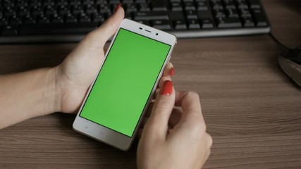 Woman looking at smartphone phone with green screen sitting at office desk. Business woman using a Smart phone. 4K UHD. Close up.