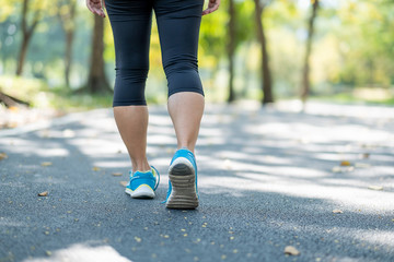 young fitness woman legs walking in the park outdoor, female runner running on the road outside, asian athlete jogging and exercise on footpath in sunlight morning. Sport,healthy and wellness concepts