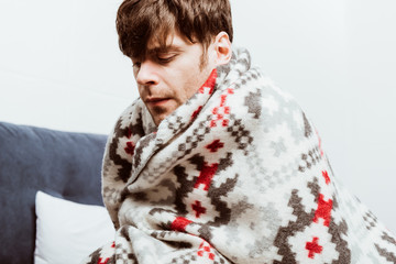 Wall Mural - sick young man wrapped in blanket sitting on bed at home