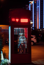 Spaceman Standing In A Telephone Box At Night